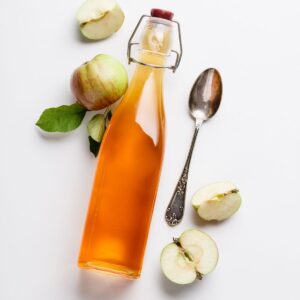 a tablespoon with a bottle of apple cider vinegar and apples